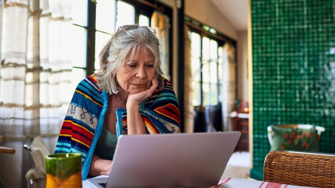 How does the UK state pension compare with other countries? Old lady with grey hair sits at home with a brightly coloured blanket around her shoulders, looking at her laptop