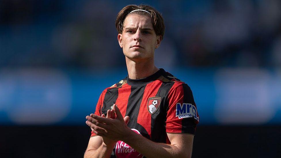 Alex Scott, wearing Bournemouth's red-and-black-striped home kit, applauds fans after a match at Manchester City