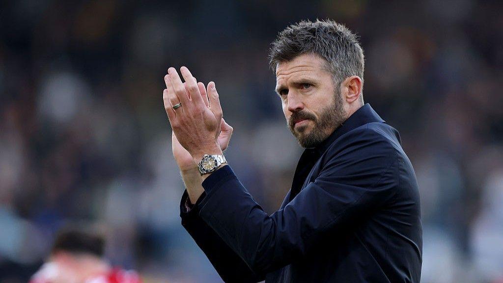 Manchester United head coach Michael Carrick applauding, wearing a dark jacket