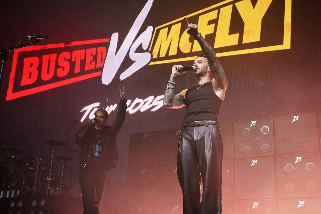 Charlie Simpson and Matt Willis from busted stood in front of a screen that reads "Busted VS McFly Tour 2025"