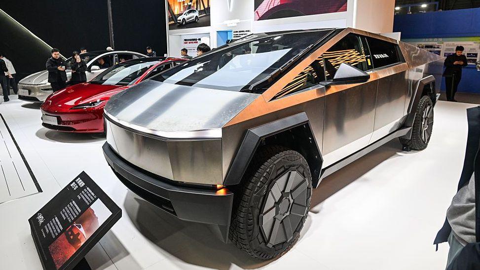A series of Tesla electric cars on a show floor, including the angular Cybertruck in the foreground.