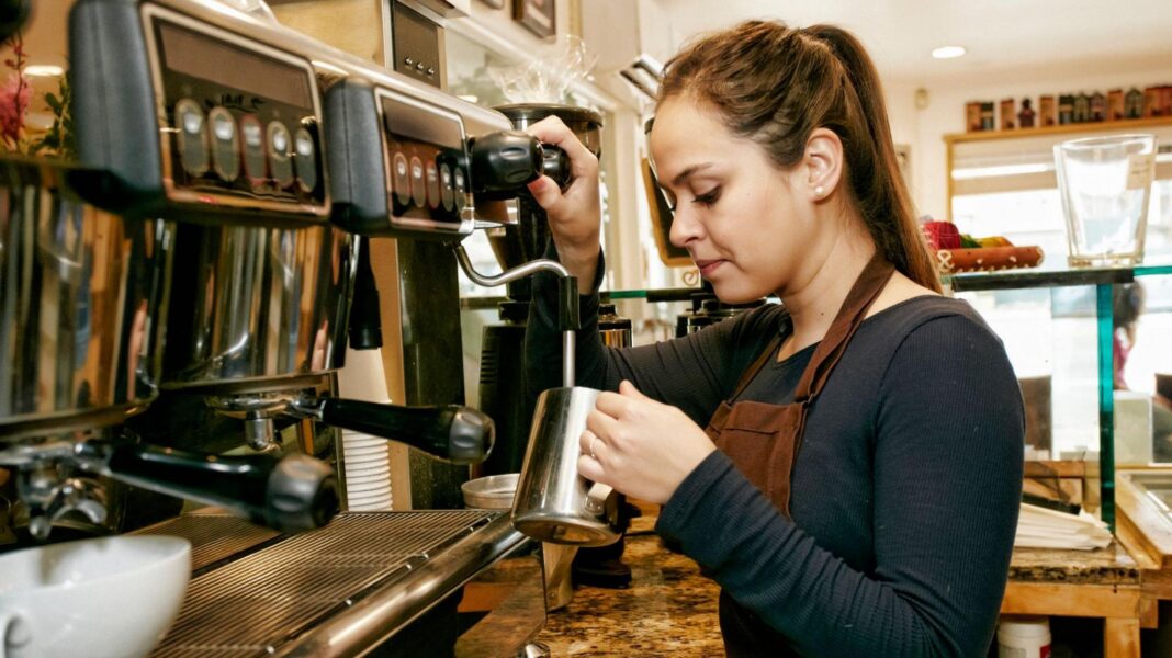 A young female wearing a black top and operating a coffee machine in a shop