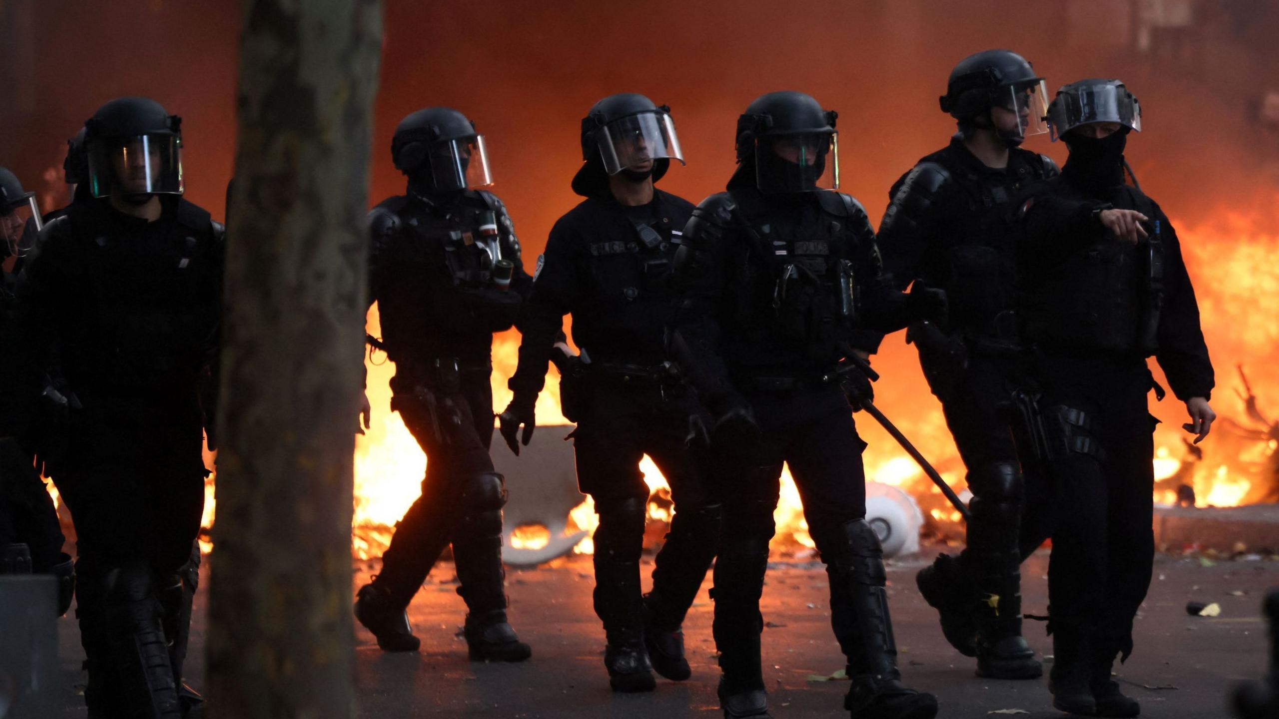 French riot police walk past a burning barricade amid clashes with protesters during a day of demonstrations on 17 October