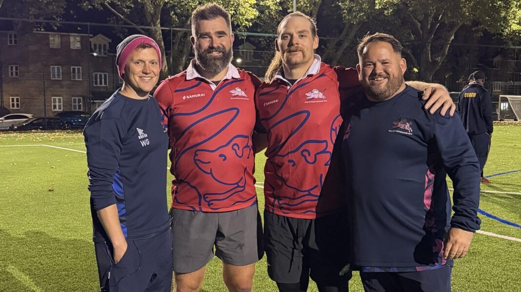 Jason Kelce and Beau Allen with arms round each other and two members of Old Streetonians RFC staff on training pitch under floodlights. Both NFL players are wearing red playing tops.