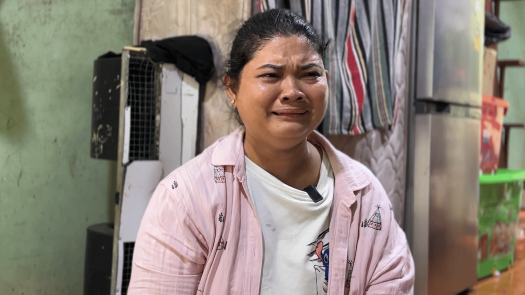 Young men live in fear of being snatched off the streets and sold to Myanmar’s army A woman wearing a white t-shirt under a pink overshirt grimaces in pain. Behind her is a wall, a fridge, a mattress resting vertically against the wall and some colourful boxes stacked on top of each other
