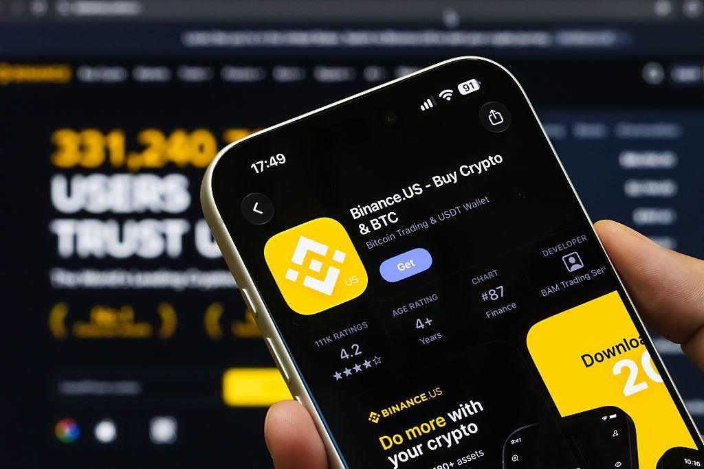 A phone with the Binance.US app on it next to the yellow logo
