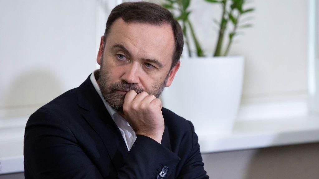 Close up of Ilya Ponomarev leaning his chin on his hand in a photo taken in 2022. He has short dark hair, facial hair and is wearing a dark jacket and white shirt.