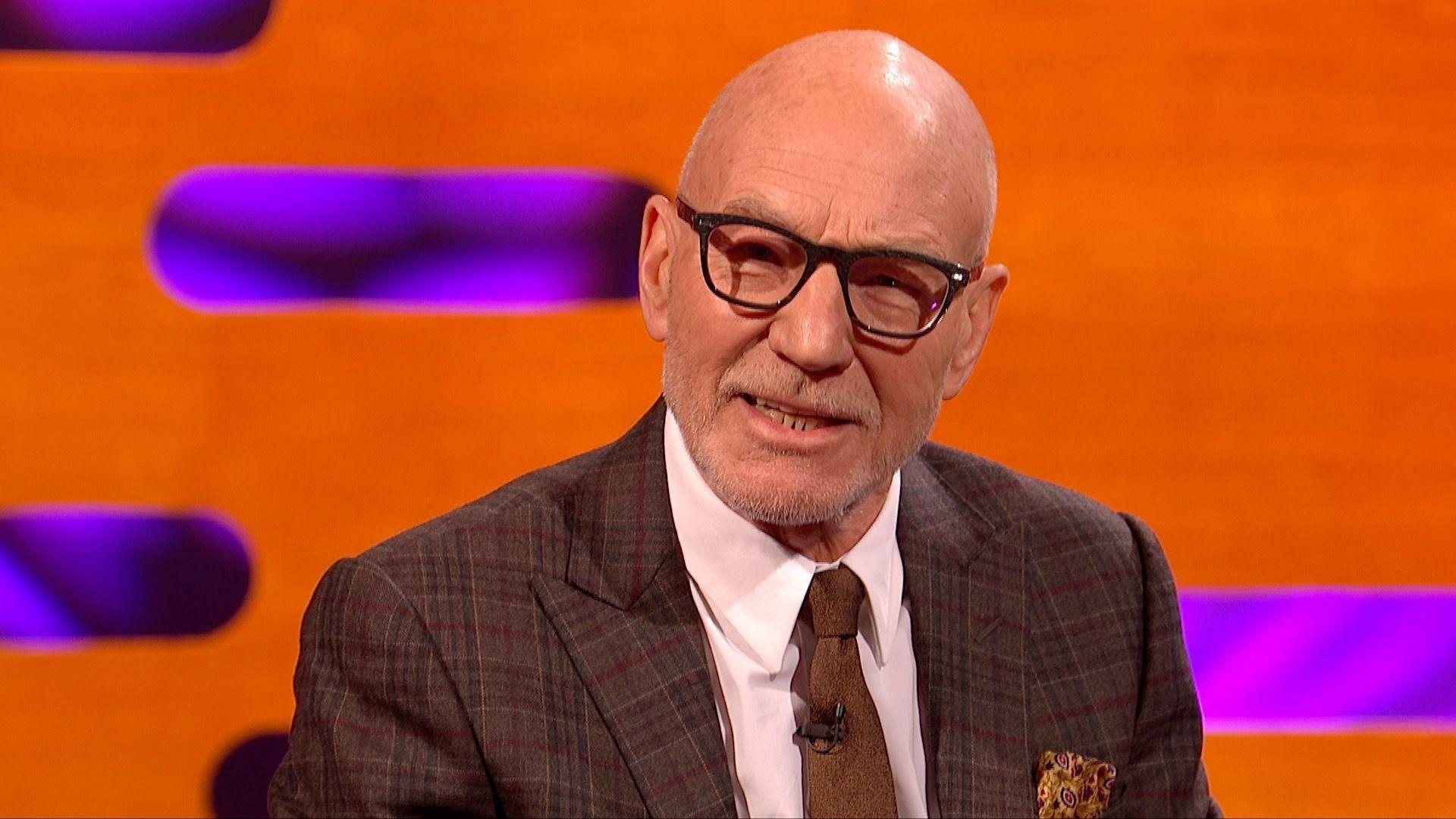 A man with glasses in a suit and tie sitting in a bright orange studio.