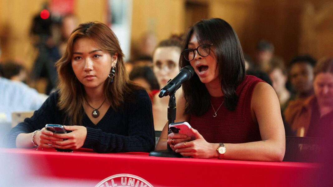 Two students speak into a microphone while sat at a table in front of a crowd in a hall address an assembly on sexual violence held at Cornell on Thursday