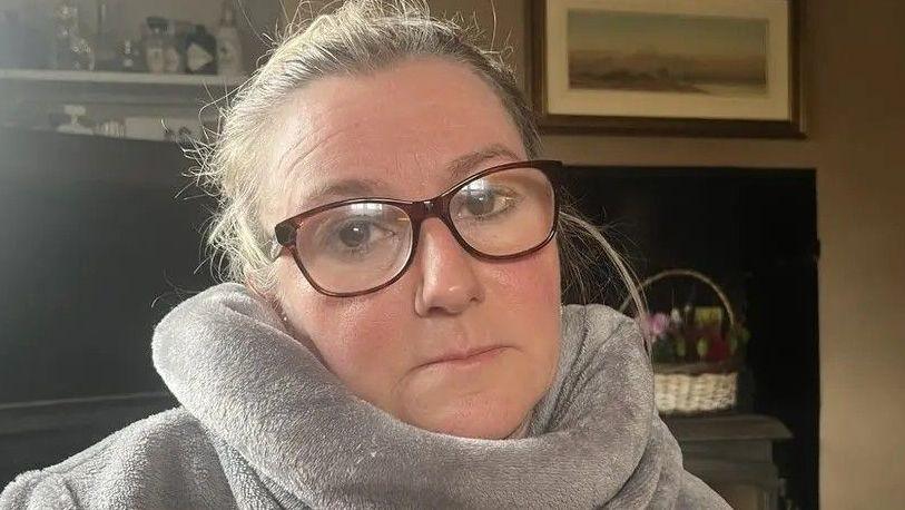 Woman's head. She is wearing glasses and has a large, cushioned collar around her neck which appears to be part of a larger towelling top that also covers her shoulders.