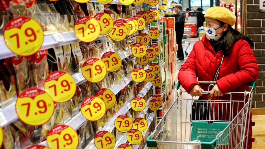 China’s economic growth picks up as AI boom boosts exports A customer wearing a mask and winter jacket browses through products at a supermarket in Lianyungang, in eastern China's Jiangsu province on January 9, 2025. She is standing in an aisle with a trolley in front of her, flanbked by shelves with yellow-colour discount promos on them.
