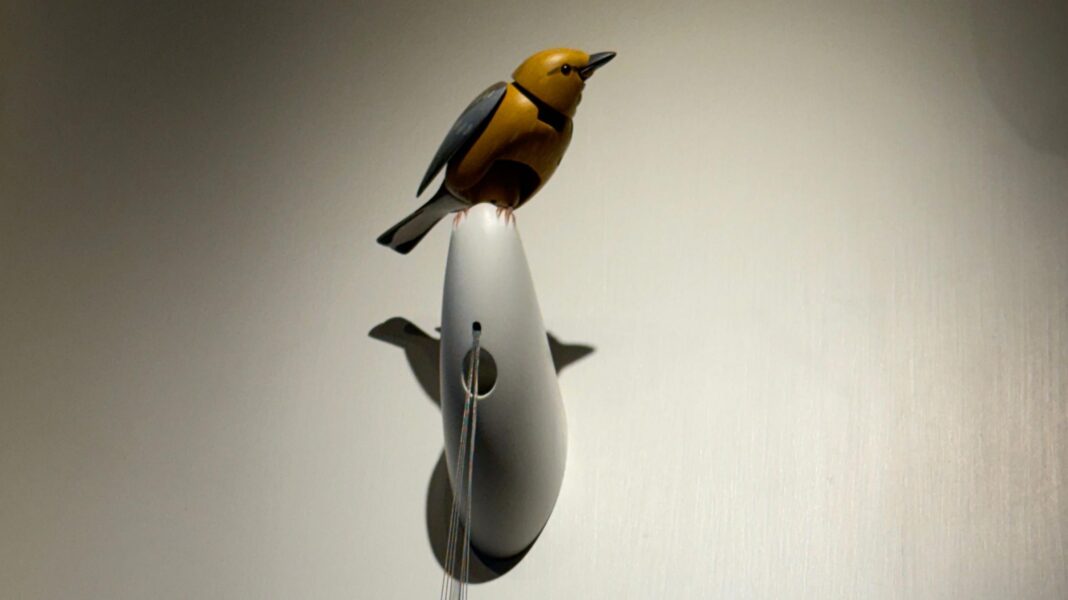 A wooden mechanical bird sits on a white perch