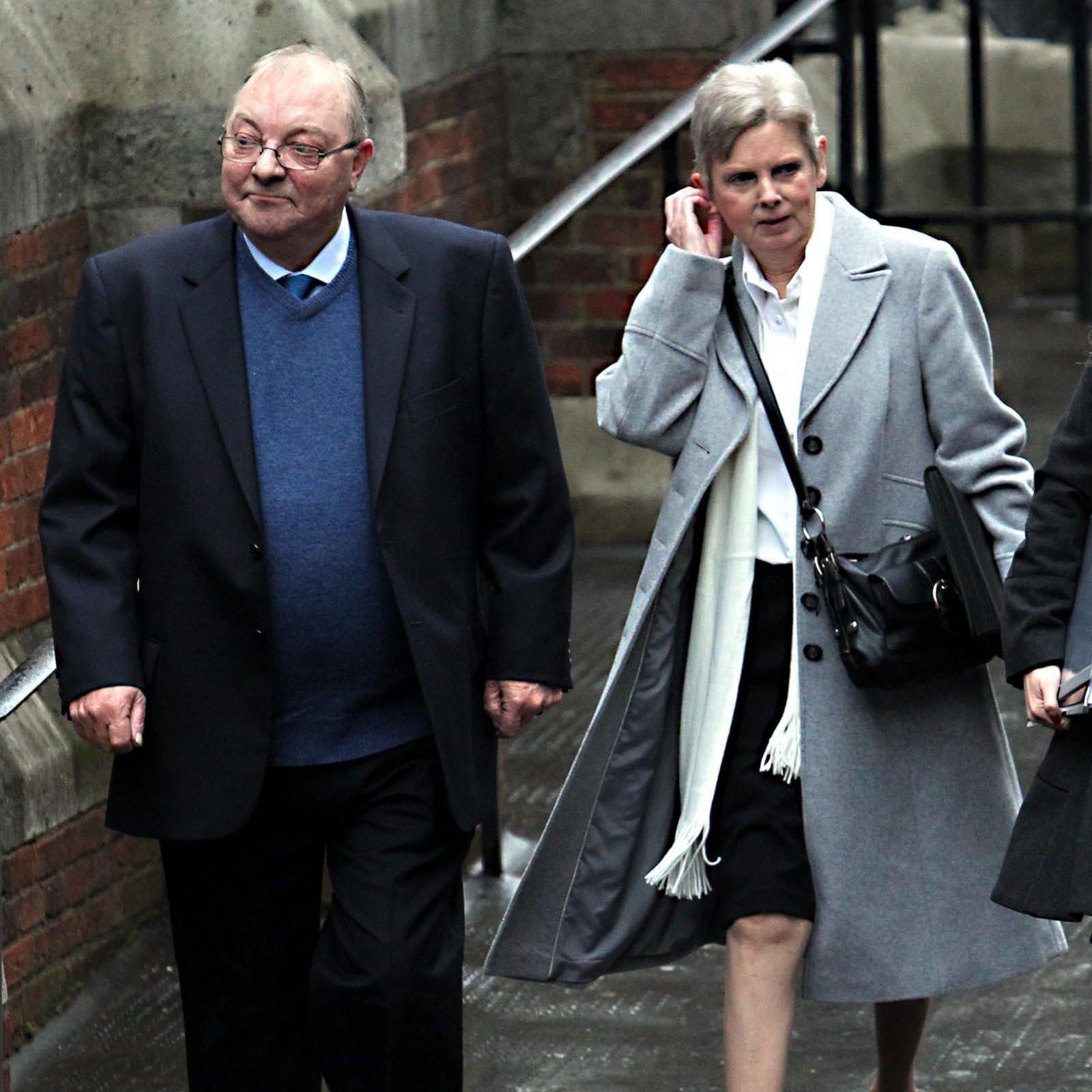 Margaret Watson arrives to give evidence with her husband Jim to the Leveson Inquiry at The Royal Courts of Justice, The Strand, London. Two people walking outdoors beside a brick and concrete building, with one wearing a dark coat and blue jumper and the other wearing a light grey coat and carrying a shoulder bag.