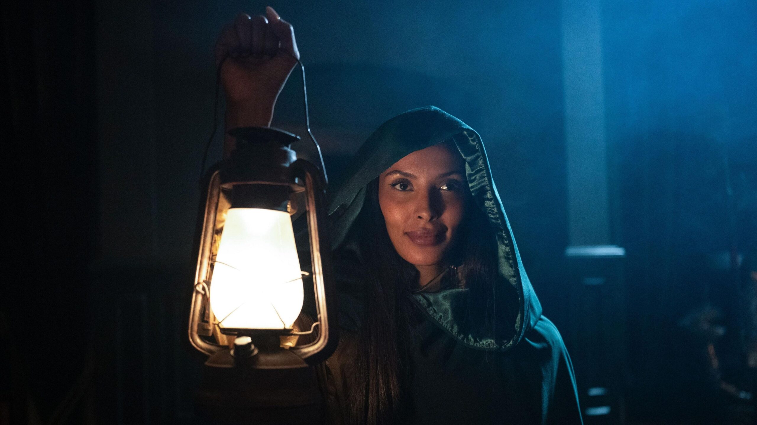 Maya Jama wearing a green cloak and holding up a lit lantern on the Celebrity Traitors.