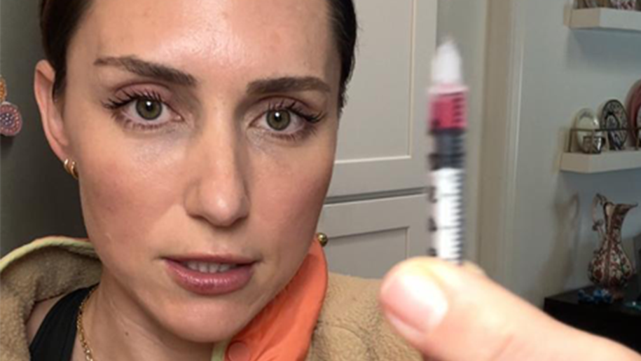 Katie, a woman with brown hair in a ponytail is holding up a syringe and injecting the peptide GHK-Cu into her bum cheek