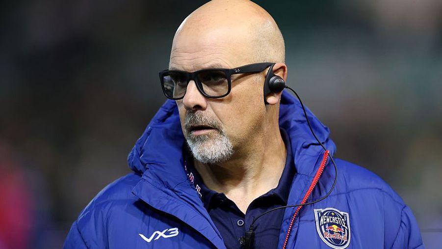 Dan McFarland wearing a hybrid pair of glasses/sunglasses and a blue Newcastle Red Bulls puffa jacket