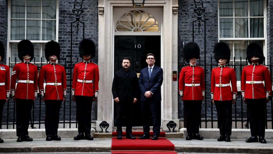 Ukrainian President Volodymyr Zelensky and UK Prime Minister Andy Burnham standing in front of No 10 Downing Street. They are standing on a red carpet. On either side of them are soldiers from the Number 12 Company of the Irish Guards, wearing scarlet tunics and bearskin hats.