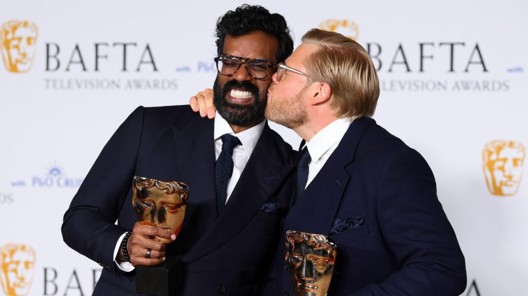 Romesh Ranganathan and Rob Beckett posing at the 2024 Baftas. Rob is kissing Romesh on the cheek