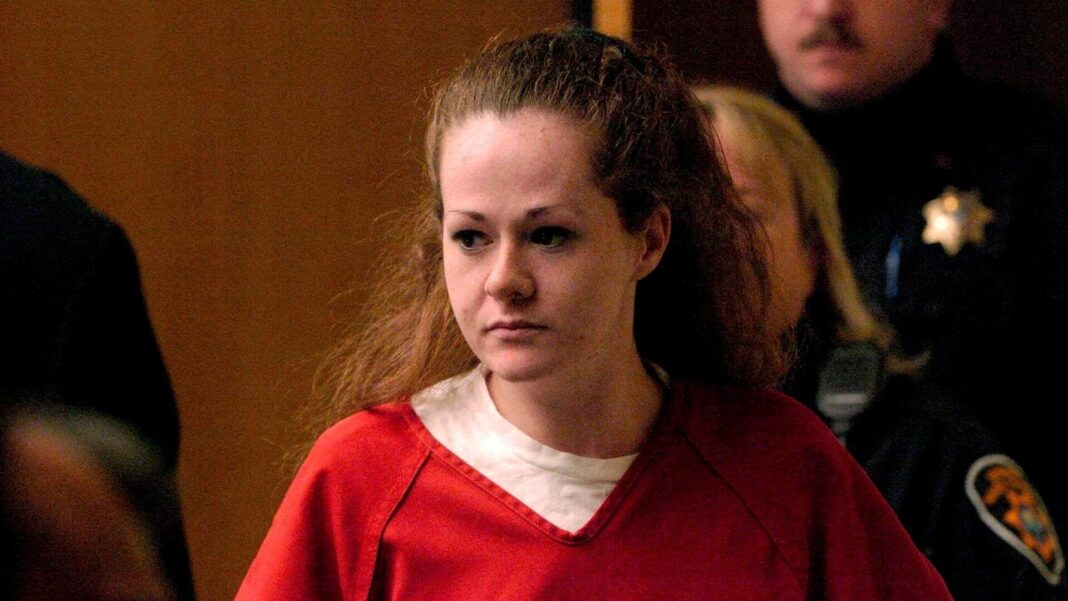A woman with red hair wears a red jumpsuit