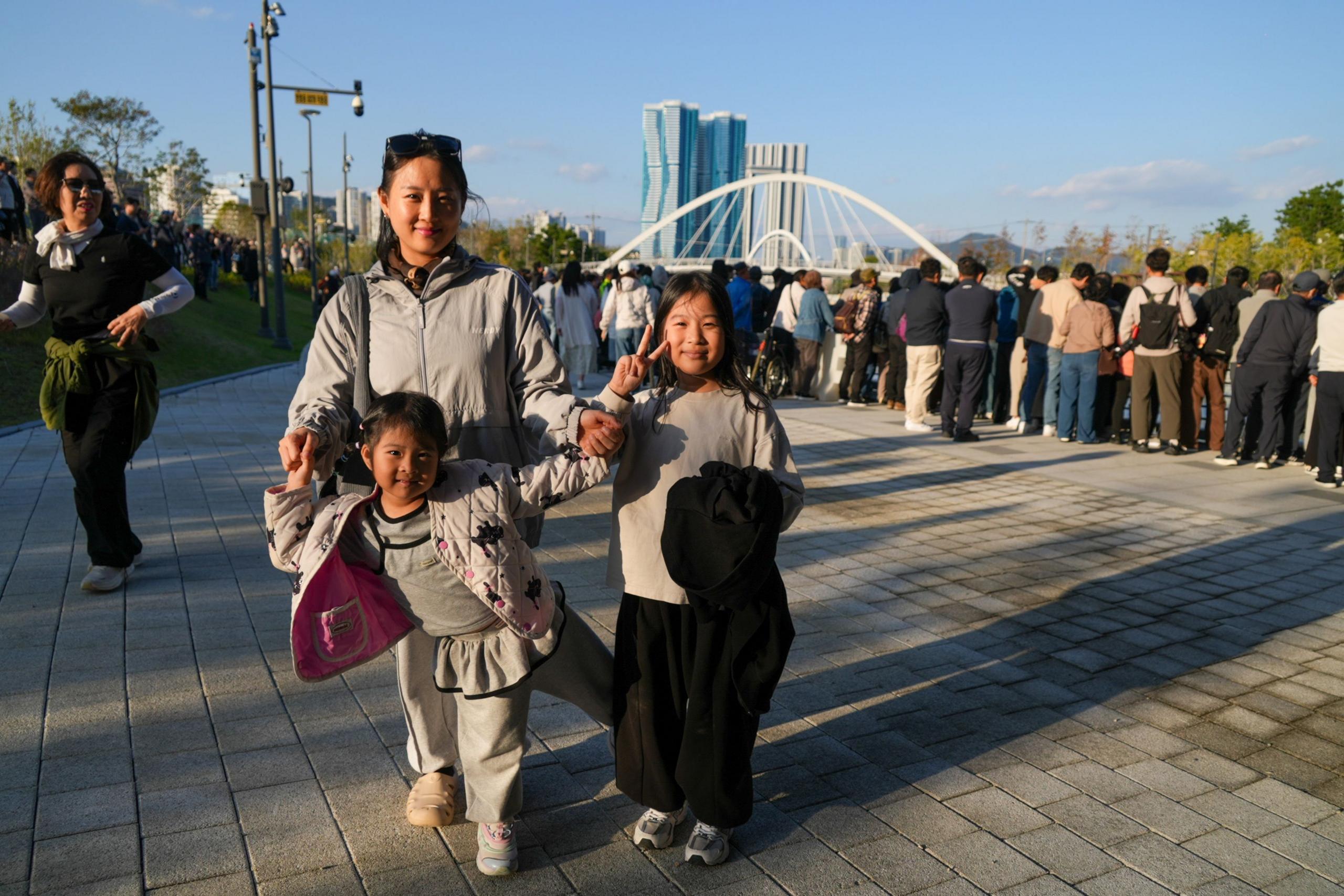 A family of three smiling at the camera as a crowd gazes into the canal watching Bukangi.