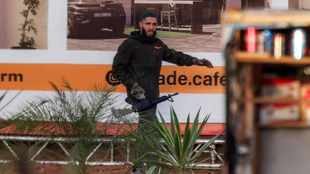 A gunman carrying an assault rifle walks near a billboard.