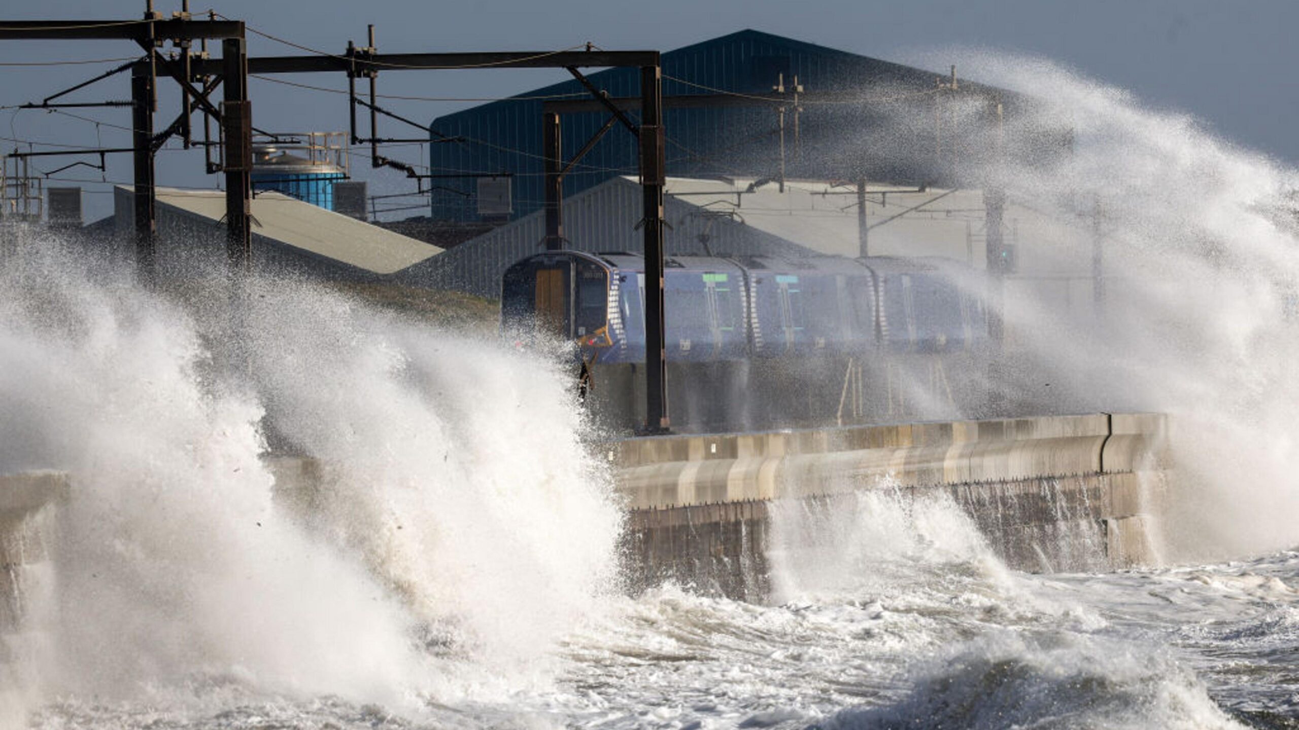 Waves batter coastal defences and crash onto a passing train