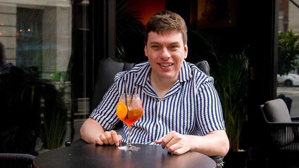 Alex waiting outside a bar with a cocktail
