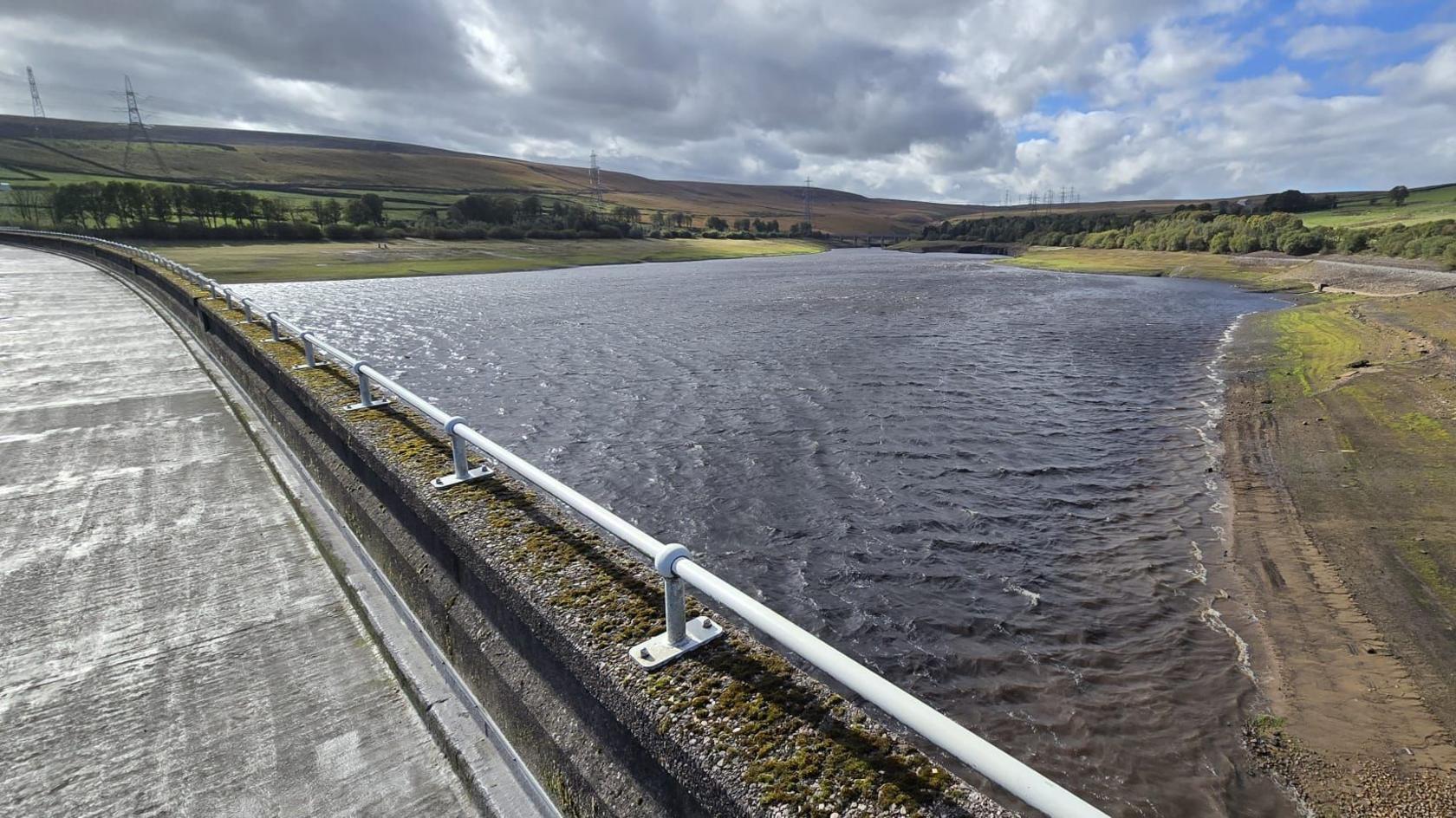 A reservoir with a low water level and hills in the background.