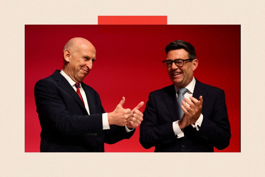 John Healey and Andy Burnham. Healey is doing a thumbs up with both hands and Burnham is clapping. They are wearing suits and are standing in front of a red background.