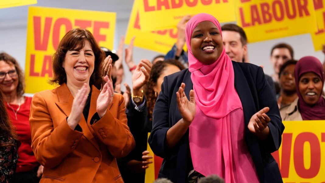 Labour sees off Green challenge to win Holborn by-election Lucy Powell is wearing an orange jacket over a black top. Sagal Abdi-Wali is wearing a navy jacket and a pink hijab. Both women are clapping and smiling. They are standing in front of supporters, some of whom are holding yellow and red signs reading: 'Vote Labour'