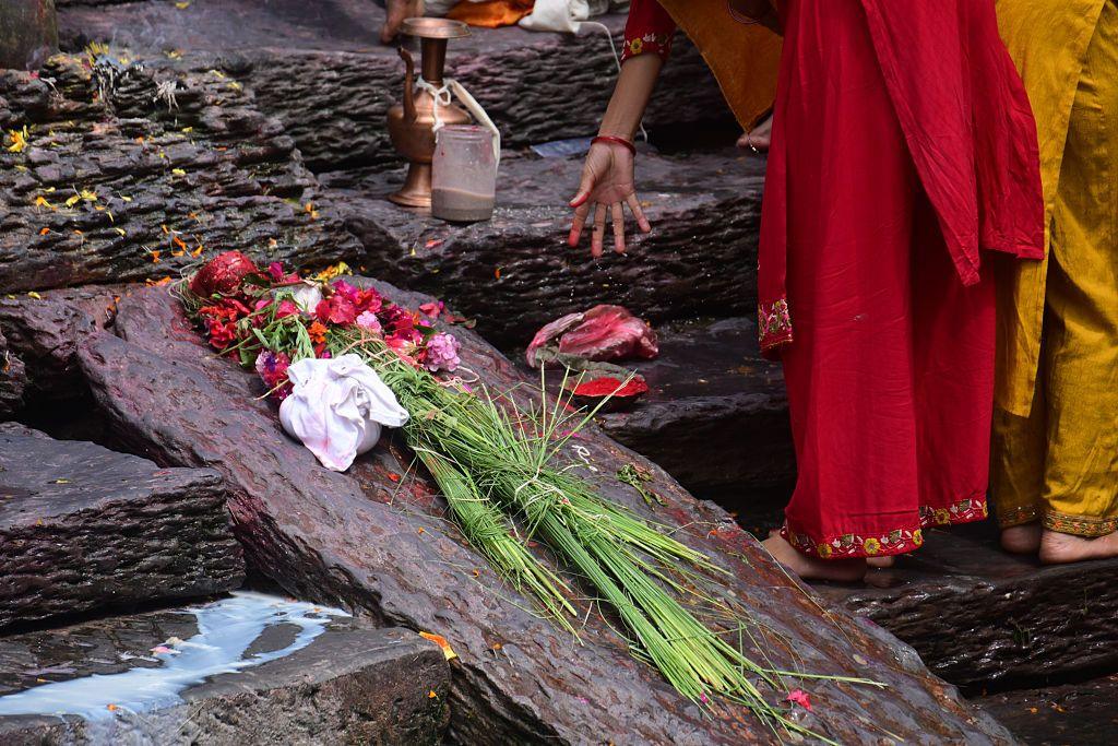 Holy grass kusha laid out on a stone with flowers. Two women are standing next to the stone - their faces are not visible.