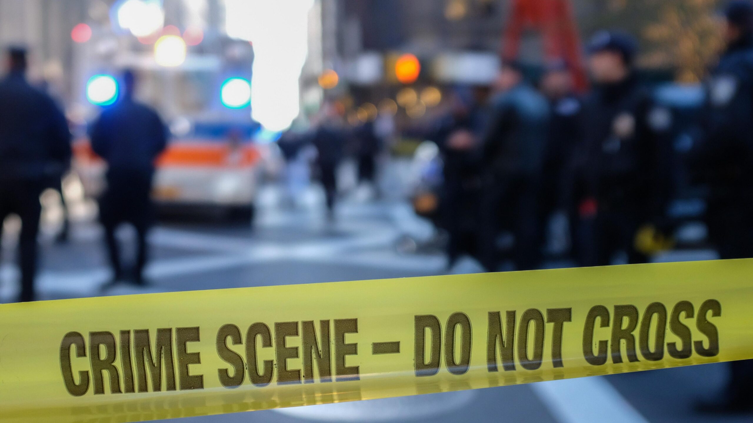 Police sealing off a US city street with yellow tape reading "crime scene - do not cross".