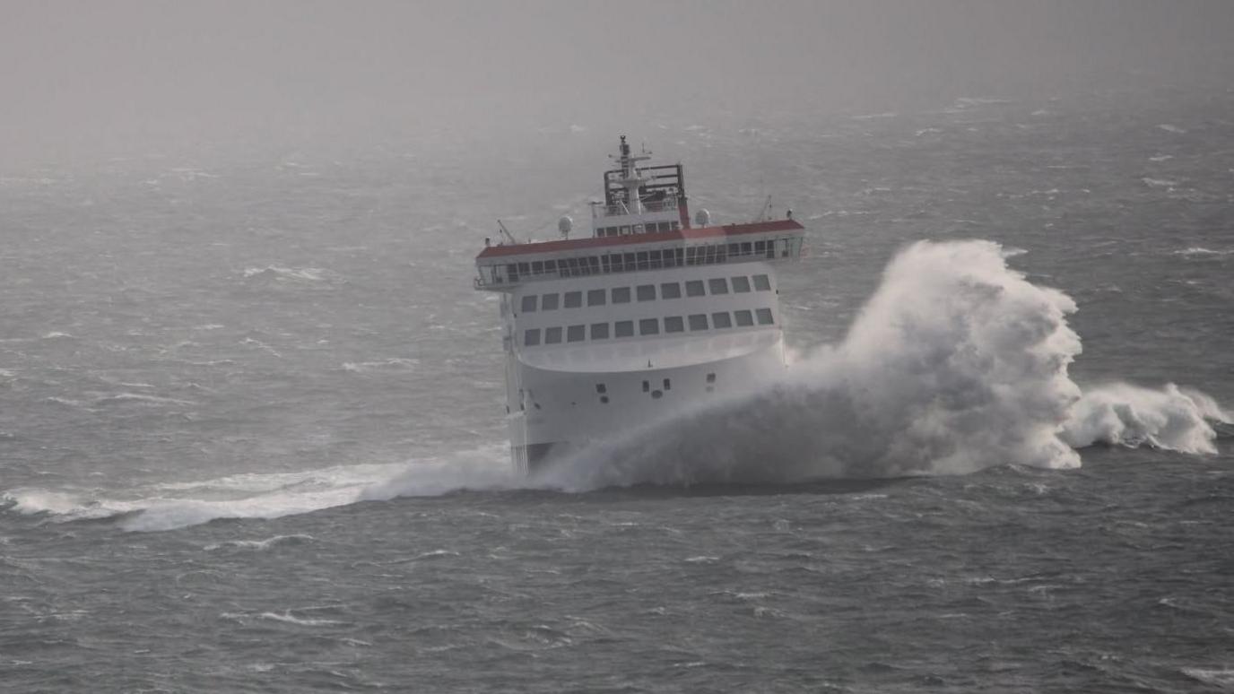 The Manxman ferry at sea on a choppy grey day with huge waves and white horses splashing to the right.