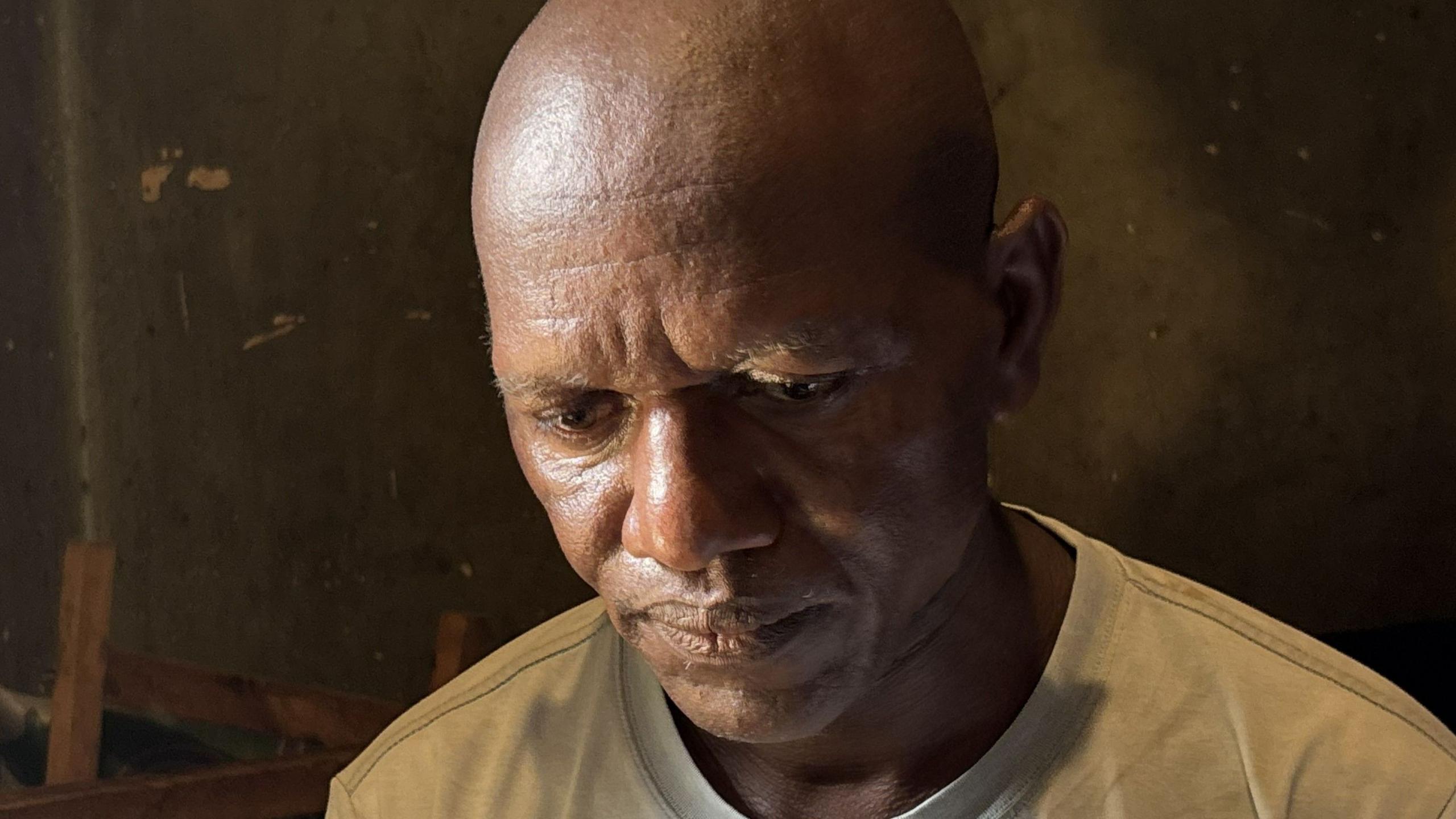 A close-up shot of a bald man wearing a white T-shirt looking down