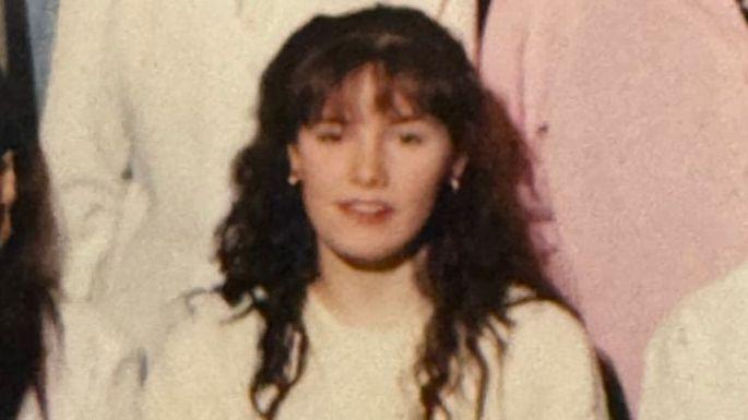 Cropped group photograph showing Pauline with long curly hair wearing a light-coloured top, looking towards the camera, with other partially visible people standing nearby.
