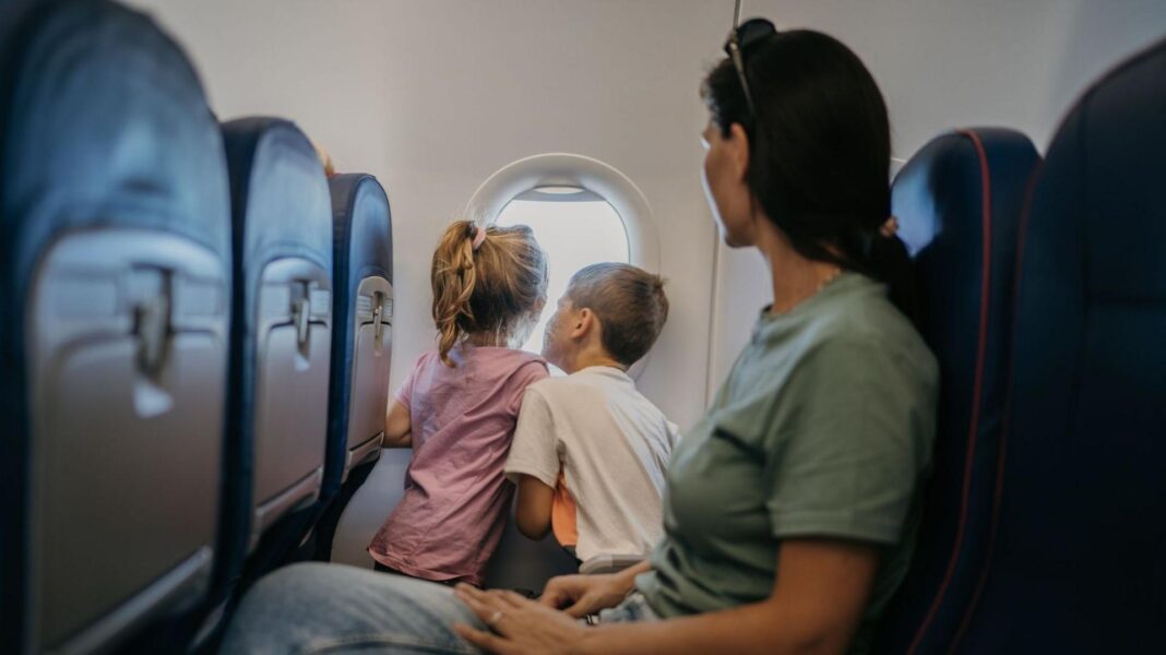 A dark-haired woman watches on as two children look through an aeroplane window.