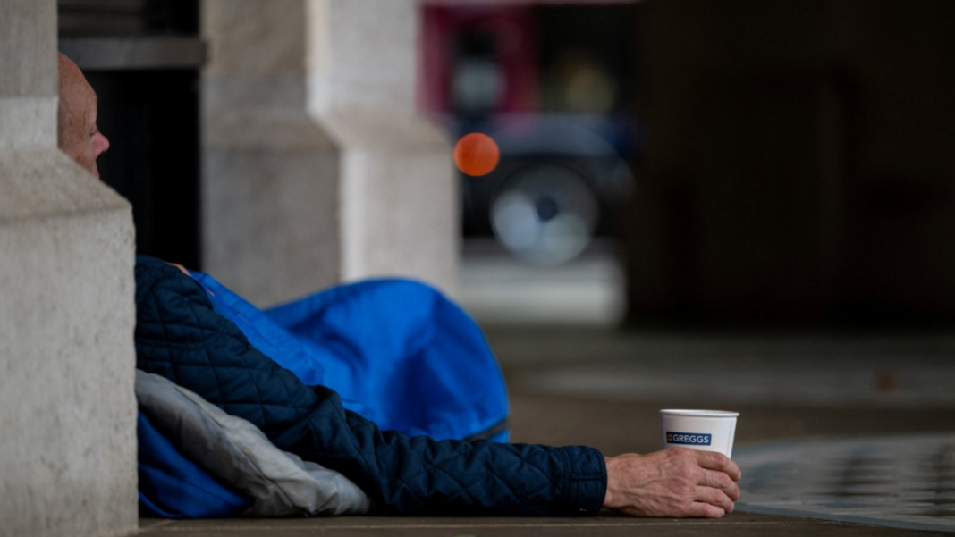 Funding set to double for plan to get rough sleepers off streets by Christmas A homeless person lies in a London doorway in a blue sleeping bag. Part of the man's face is visible around the corner of a building and he is holding a paper cup.