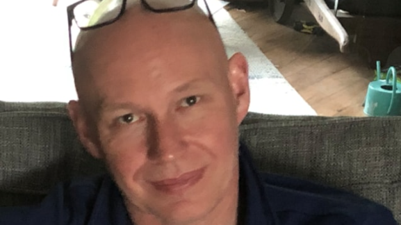 Michael Mullins shown with sitting on a sofa with his glasses resting up on his forehead