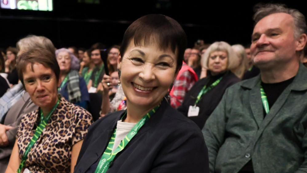 Caroline Lucas smiling while sitting in the audience at a party conference