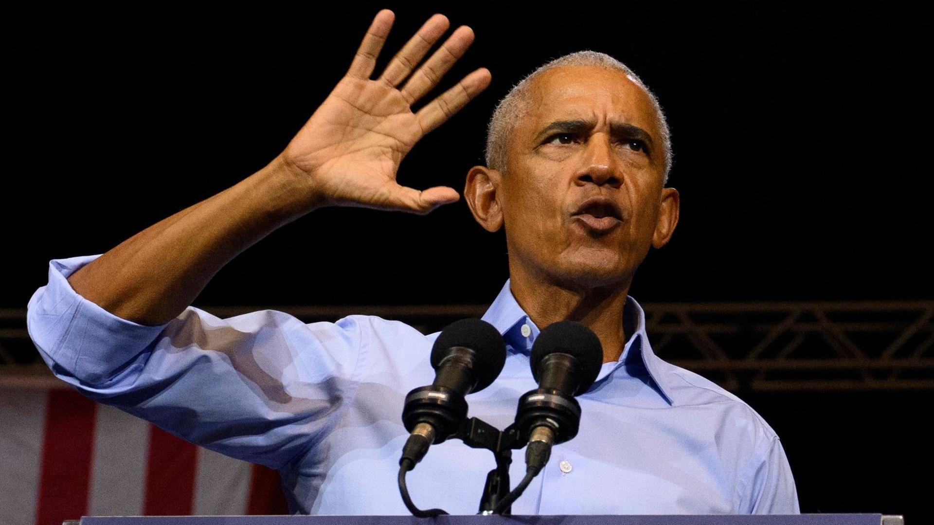 Obama gestures as he speaks at a podium wearing a blue shirt