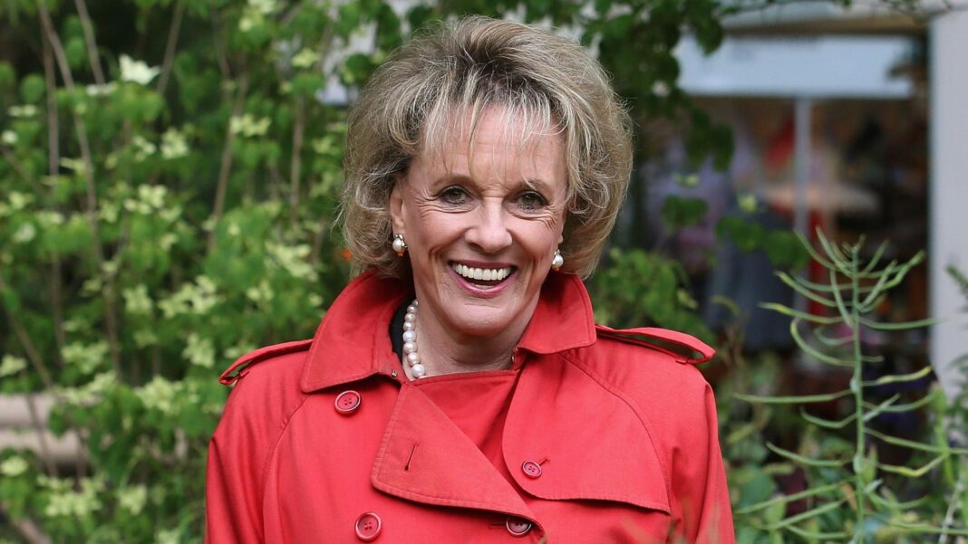 Rantzen felt ‘deprived of choice’ over her own death Head shot of Dame Esther Rantzen looking at the camera smiling. She's wearing a red coat, with pearl earrings and a matching pearl necklace, with green plants in the background.