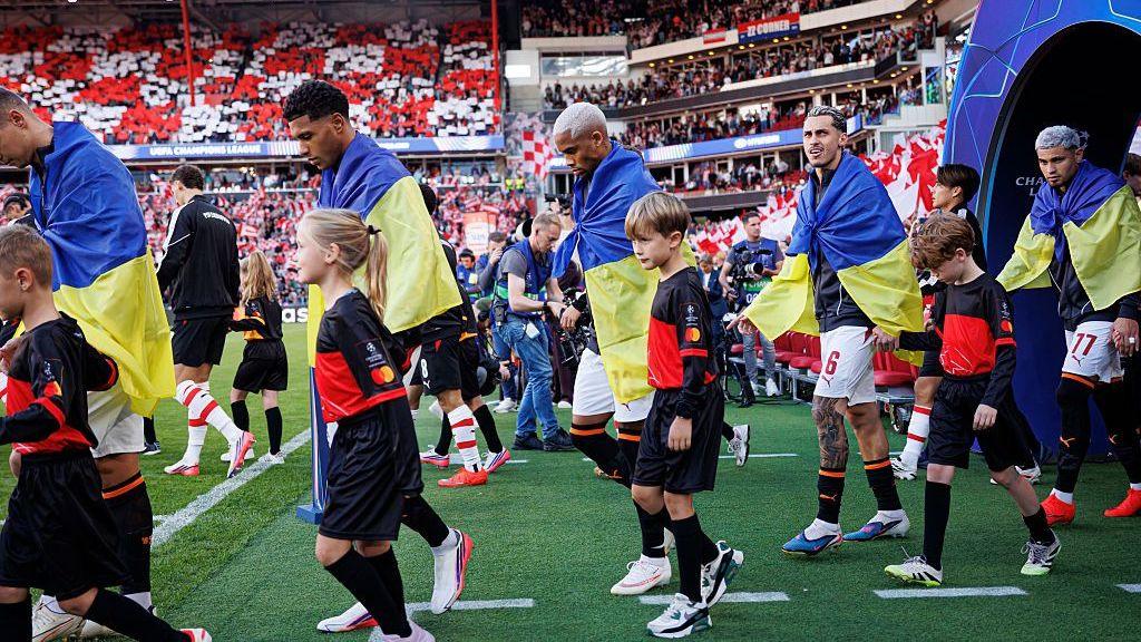 Vinicius Tobias, Pedro Henrique and Marlon Gomes of Shakhtar Donetsk enter the pitch prior to a Champions League game, draped in Ukraine flags