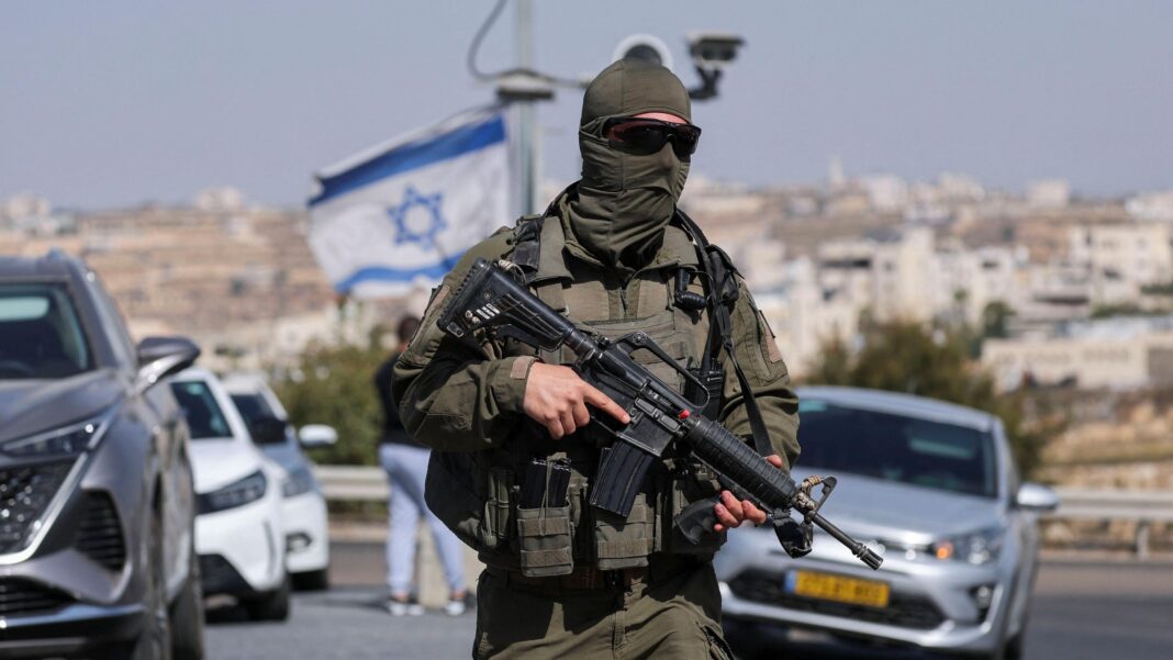 A masked Israeli soldier stands holding a gun