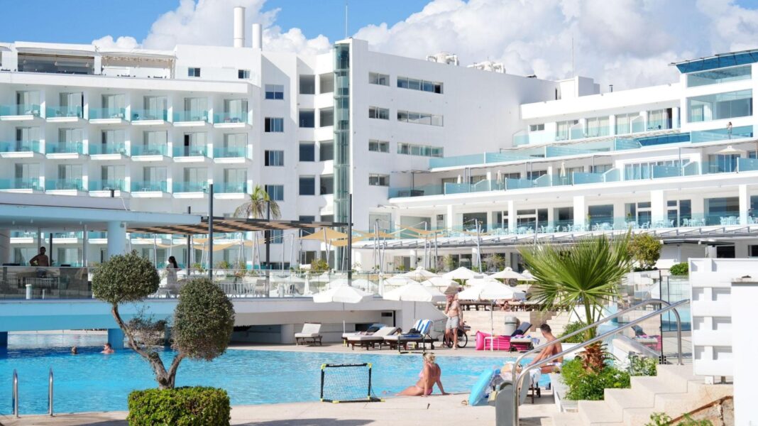 Dad saw son, 2, fall to death from Cyprus hotel window, court hears People lounging by a swimming pool at the hotel, which is a large white building with various balconies on its front.