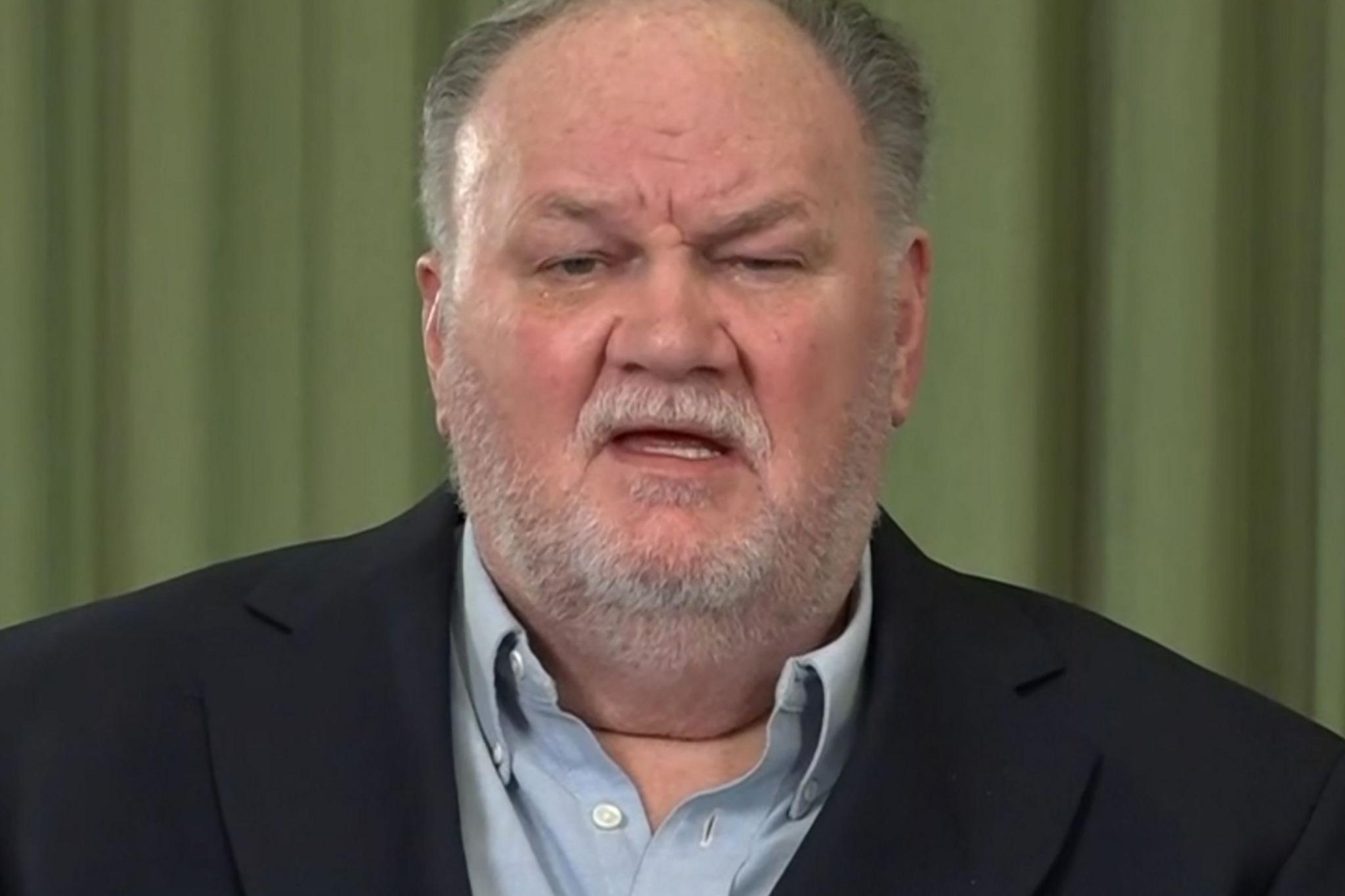 Close-up of Thomas Markle Sr wearing a dark blazer and light blue shirt, against a green curtain backdrop