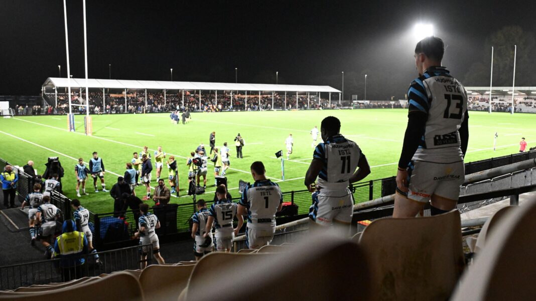 Players walk out onto the St Helen's pitch at night with floodlights lighting up the pitch