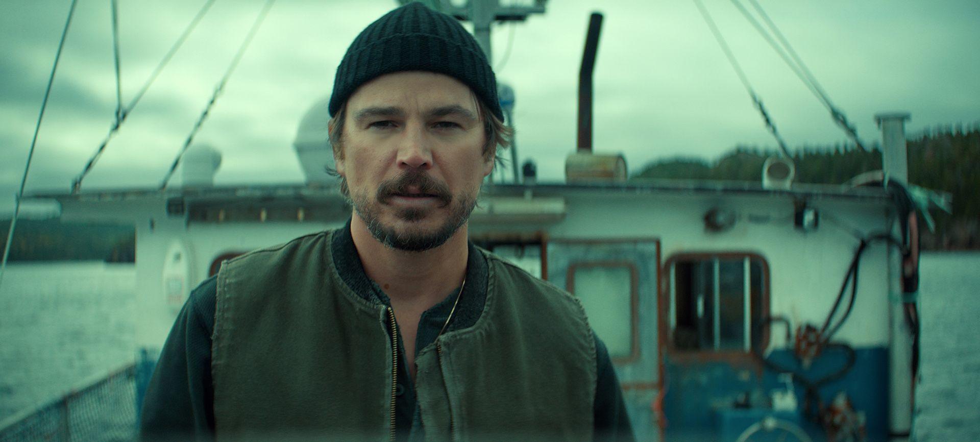 A production still from the show that depicts Josh Hartnett looking at camera on the deck of a small fishing boat against a moody cloudy grey sky.