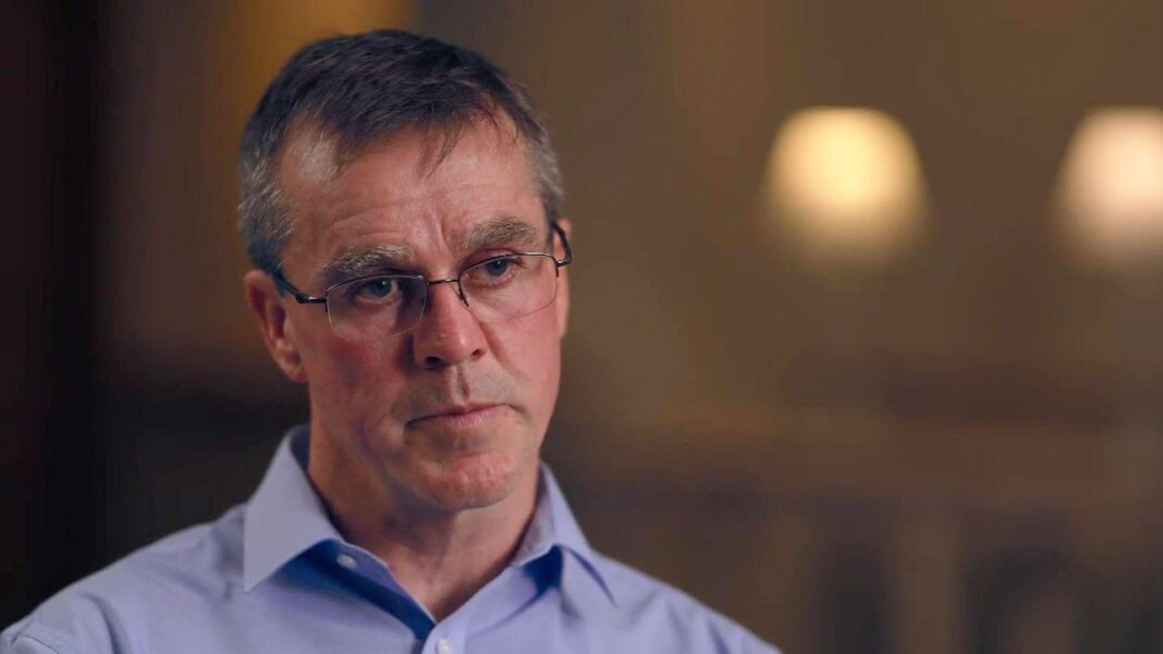 Dr Stephen Brearey, wearing thin-framed glasses, has short grey hair. He wears a light blue, open-necked shirt. He has a serious, neutral expression.