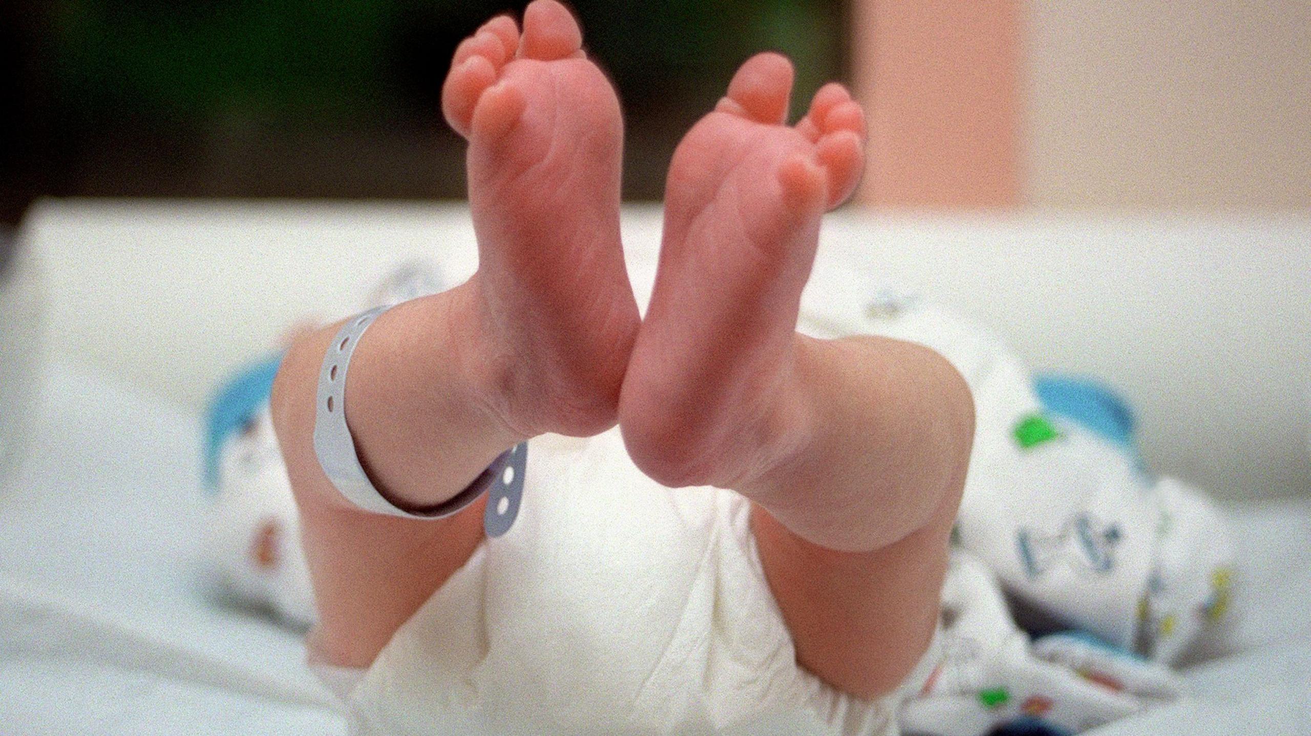 Image showing a newborn baby lying down with the soles of their feet in the foreground. The baby is wearing a nappy with a tag attached to one leg.