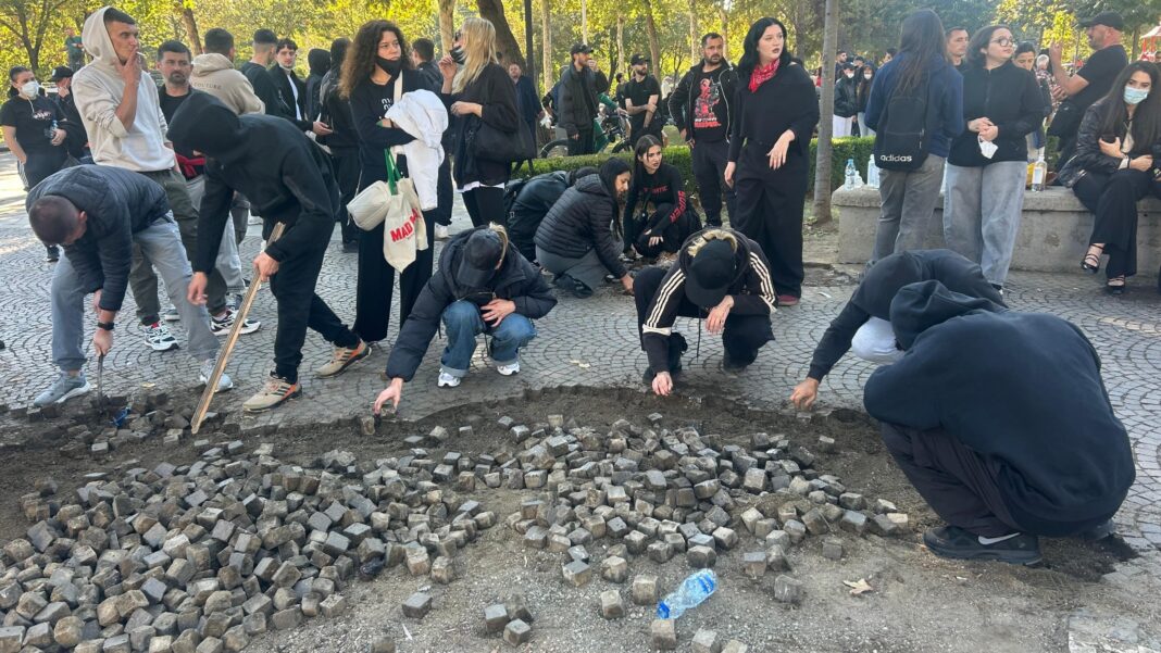 Seventh day of violent clashes between Albanian protesters and police Crouching people use hands and bits of wood to loosen cobblestones.